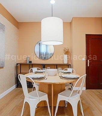 Sala com mesa de jantar de madeira e cadeiras de metal beges, aparador com um espelho preto redondo por cima